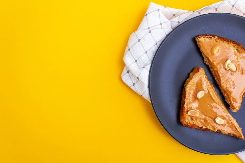 peanut butter on whole grain toast laid on a dark blue plate with a bright yellow background