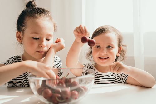 two little girls eating cherries from a clear glass bowl