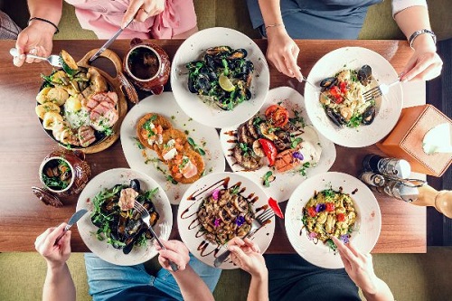 Top view of many plates of food and people eating from the plates