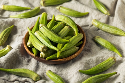 Raw Green Okra Pods in a Bunch on a linen tablecloth and in a wooden bowl