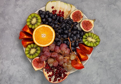 platter of fresh fruits: oranges, grapes, kiwi, persimmons, figs, pomegranate, apple on gray background. view from above
