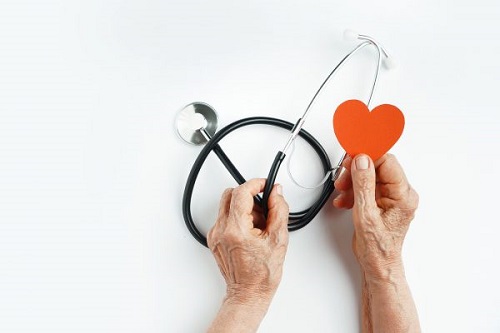 Older hands hold a stethoscope and red paper heart