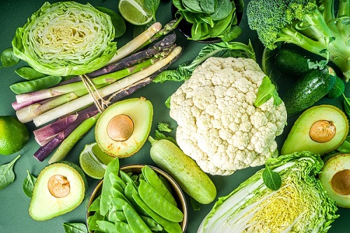 Assortment of fresh vegetables - broccoli, cauliflower, zucchini, cucumbers, asparagus, spinach, avocado, cabbage set on dark green background