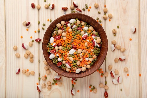 Wooden bowl filled with and surrounded by dried beans, lentils, and legumes