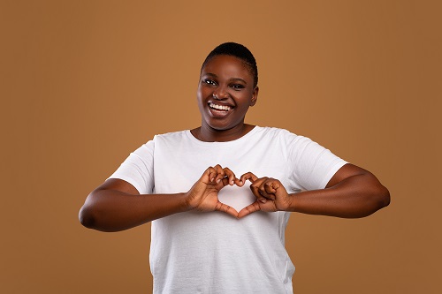 young woman in a white shirt shaping hands like heart against a brown backdrop