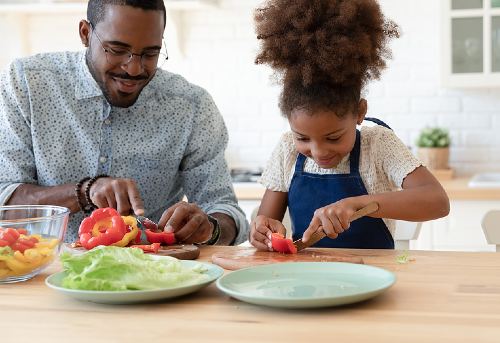 African American father and daughter cutting vegetables together 