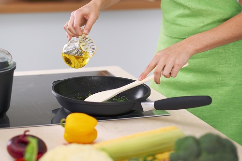 Person in green apron adding oil to a black skillet pan