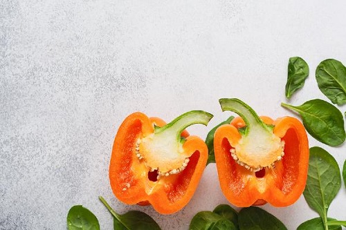 orange bell pepper cut in half in the bottom corner of a gray background