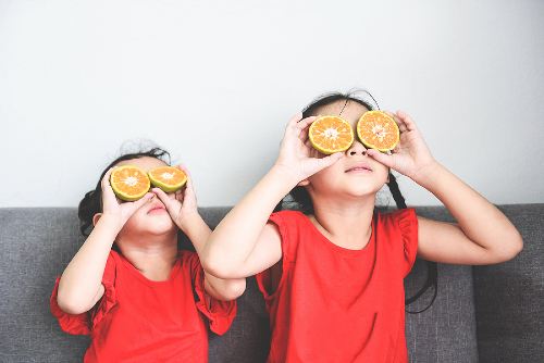 young girls placing orange slices over their eyes