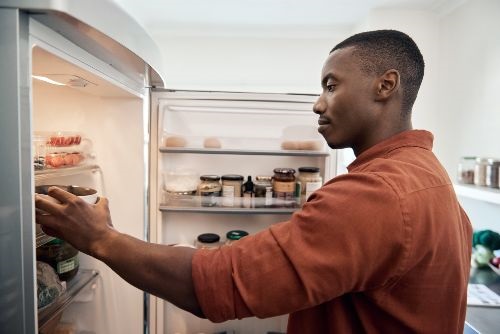 African American man reaching in an open refrigerator taking out a plastic container with food inside