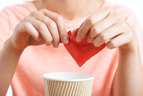 hands tearing a sugar packet over a coffee cup