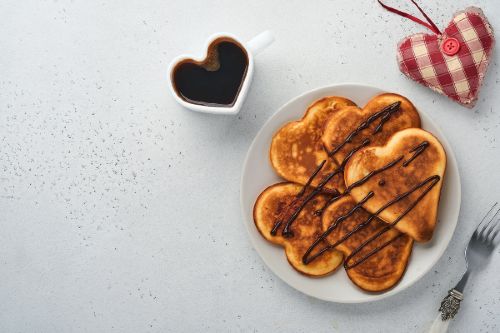 heart shaped pancakes on a white plate with a heart shaped mug of coffee and a heart shaped red and white checked ornament