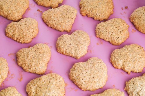 Heart shaped oat cookies lined in rows on a pink background