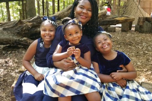 Caree Cotwright andher three daughters sitting on the ground outside in blue matching dresses