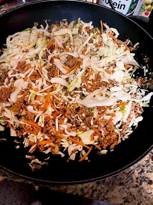a mixture of sausage, shredded cabbage, and carrots in a black wok