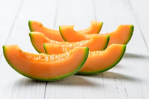 5 slices of cantaloupe with the rind still intact sitting on a light wooden surface