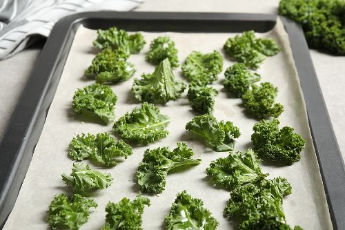 pieces of kale spread out on a baking sheet and ready to be baked into kale chips