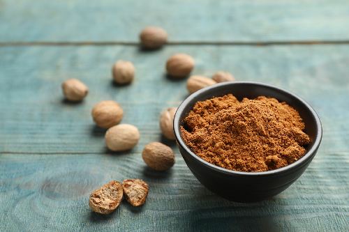 a small black bowl of nutmeg powder with nutmeg seeds scattered around it 