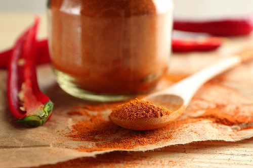 a measuring spoon of chili powder sitting in front of a full glass jar of chili powder 