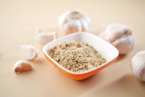 a small, orange bowl filled with garlic powder and surrounded by garlic cloves 