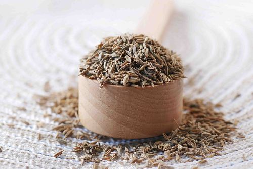 a wooden measuring cup overflowing with cumin seeds