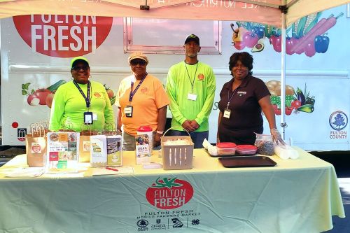 4 African American people standing behind a table with pamplets telling about Fulton Fresh mobile market on the table