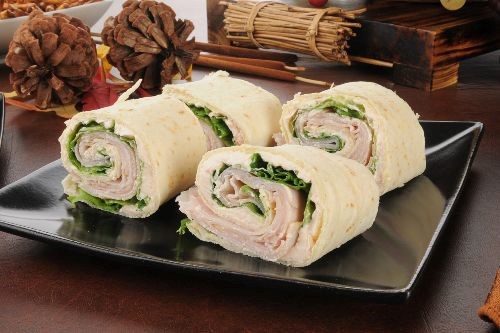 tortillas filled with turkey, lettuce and cheese rolled up and cut into 4 pieces on a black plate