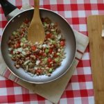 peas and rice in a pan on a white and red checkered tablecloth next to cutting board with chopped veggies