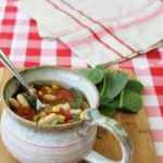 chili in a white mug with spoon on checkered cloth and wooden board