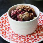 Photo shows a white bowl of fruit and crisp topping sitting on a red patterned plate.