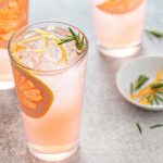 Clear classes of a light pink liquid with grapefruit slices in the glasses and a mint leaf with a dish of mint leaves and a grapefruit slice