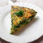 Slice of yellow and green frittata sits on a white plate