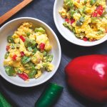 2 white bowls with eggs, red peppers, cactus, and a whole red pepper and green napkin