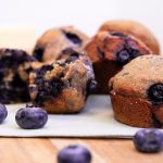 Blueberry muffins sit on a cloth napkin and surrounded by fresh blueberries