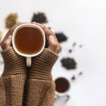 hands covered in sweater holding mug