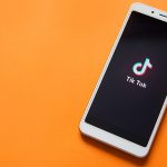 Tik tok logo on smartphone screen on orange background.