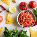 colorful bowl of salsa surrounded by chips and cilantro on a white surface