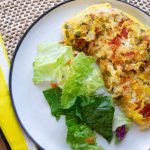 Omelet sits on a white plate next to a green salad.There is a fork on a yellow napkin beside the plate.