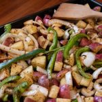 Sheet pan of red potatoes, green bell peppers, and onion slices covered in seasonings