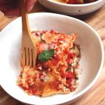 Square of Veggie Lasagna sits in a white bowl as a wooden fork pierces the corner