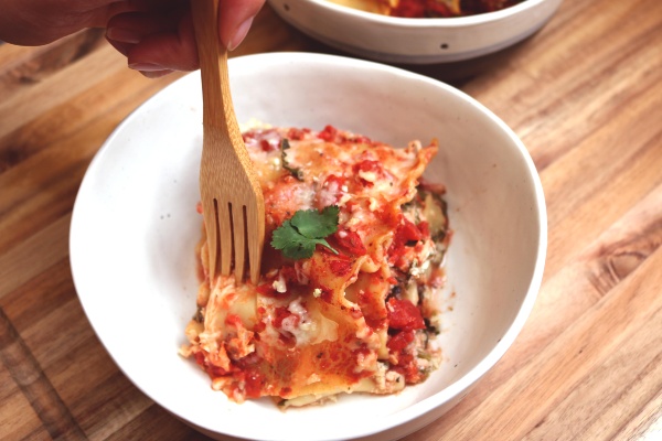 Square of Veggie Lasagna sits in a white bowl as a wooden fork pierces the corner