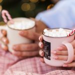 Couple sitting under a blanket both holding mugs of hot chocolate with candy canes