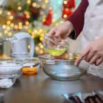 hands adding ingredients to a bowl with holiday lights in background