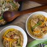 Two bowls and a skillet of spaghetti noodle dish with pieces of chicken and colorful vegetables