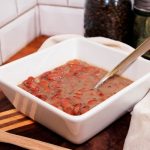 Square bowl of brown beans sits on a counter with napkins and wooden utensils