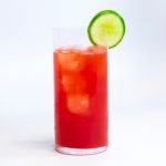 glass wit red liquid and ice in it and a lime on the rim of the glass on a white background