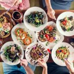 Top view of many plates of food and people eating from the plates