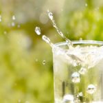 glass of water with water splashing out on a green background