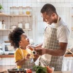 african american father and child in the kitchen wearing aprons and preparing food