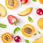 Summer background with fresh fruits and berries on white background. Set of various seasonal fruit and berry - strawberry, apricots, peach slices, cherry, mint.